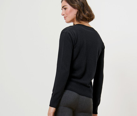 Une femme pose, portant un cardigan en maille fine avec du cachemire noir et un pantalon gris.