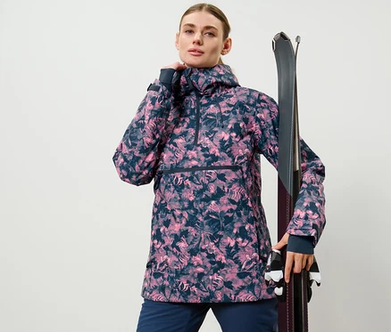 Une femme pose en veste de ski à demi-fermeture éclair avec imprimé intégral et tient des skis.