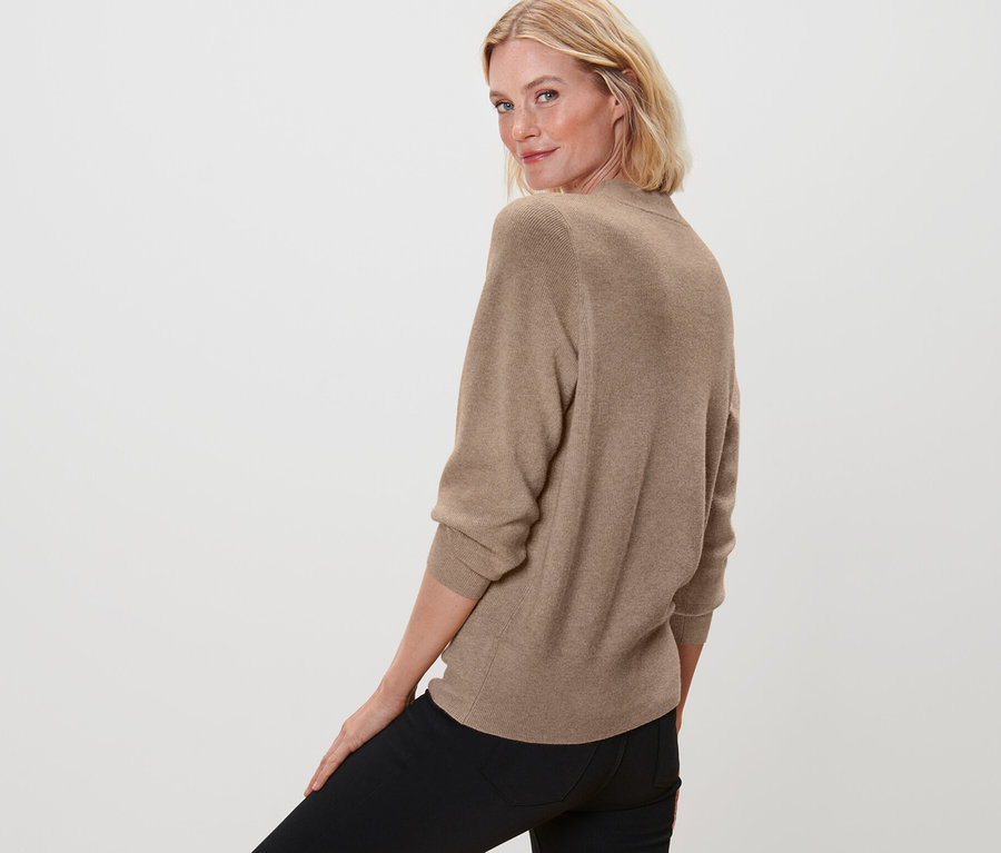 Femme regardant par-dessus son épaule et posant en pull en maille fine, beige chiné et jean noir.