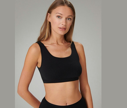 Une femme aux longs cheveux blonds porte une brassière SCHIESSER noire et regarde devant elle.
