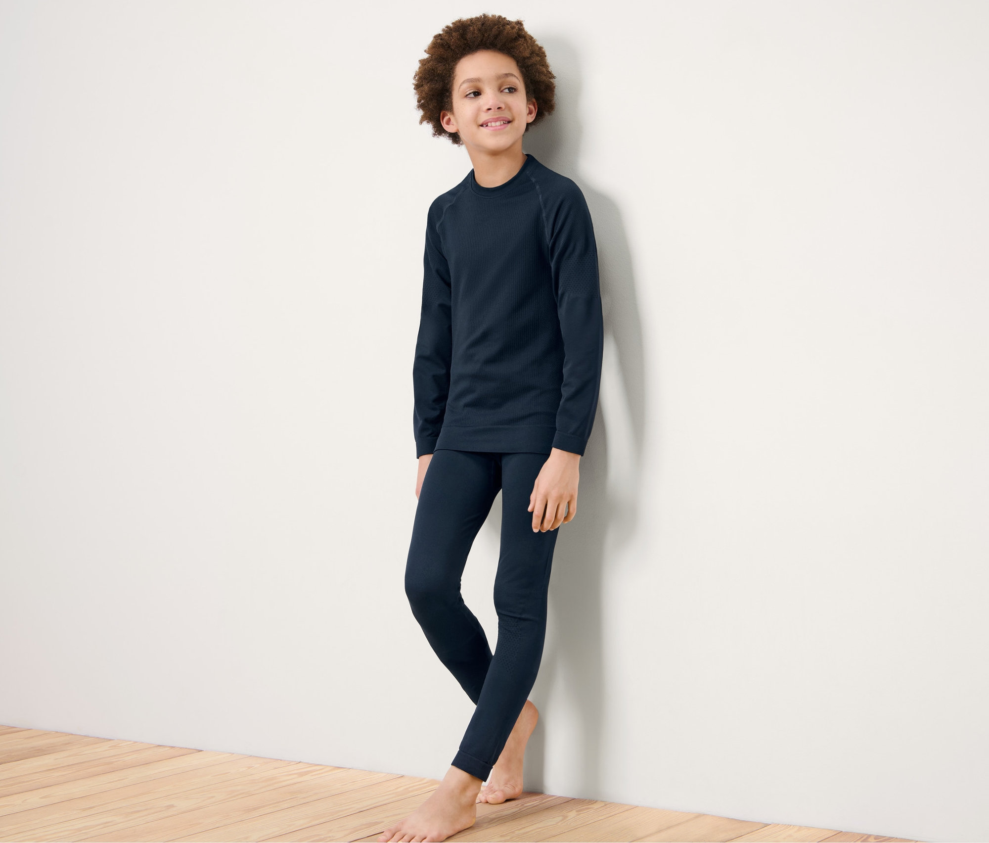 Un garçon en sous-vêtements techniques Seamless pour enfant, debout contre un mur blanc.