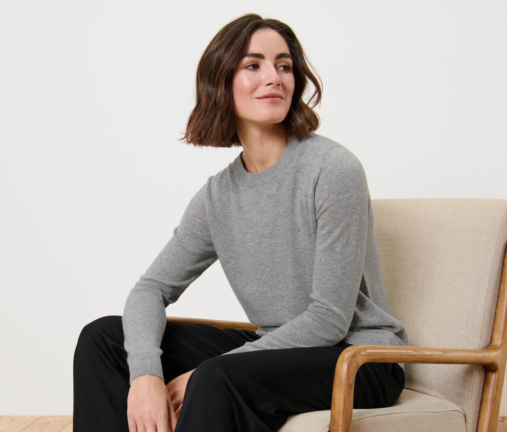 Une femme est assise dans un fauteuil et porte un pull en maille fine avec du cachemire, gris chiné.