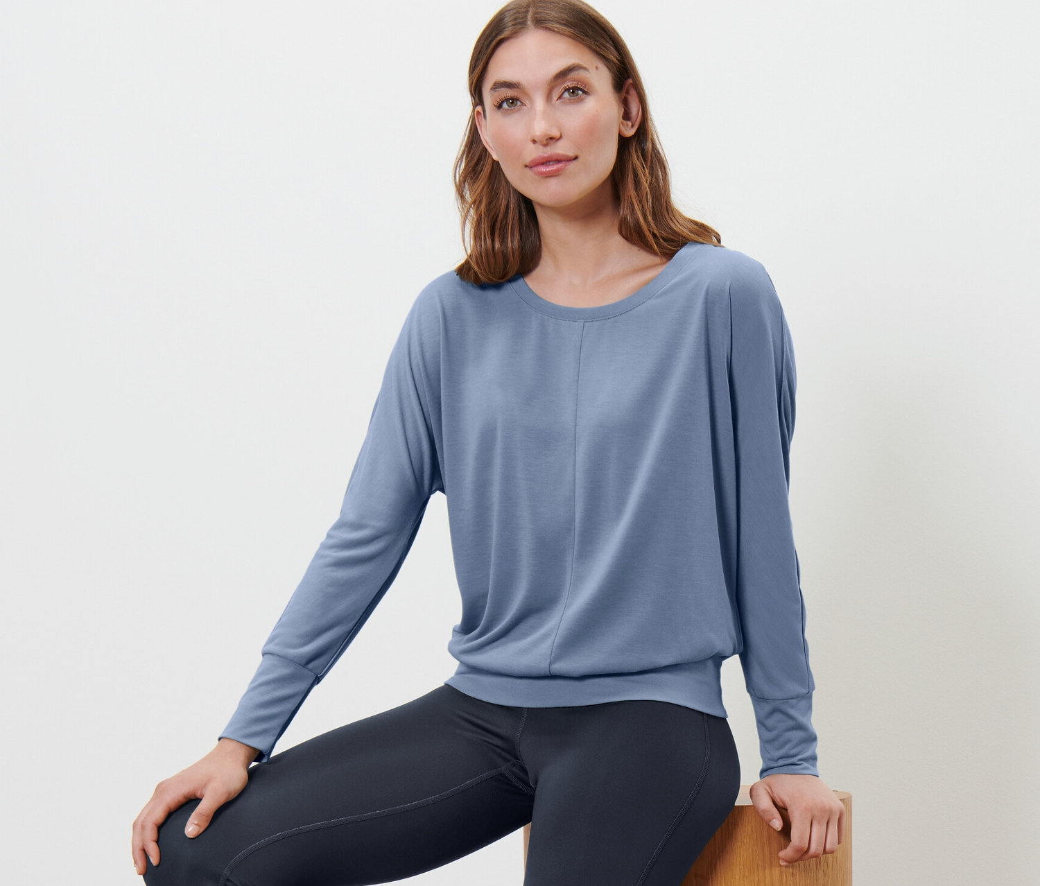 Femme assise sur un tabouret en bois portant un t-shirt de sport et de yoga bleu.