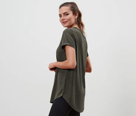 Une femme regarde par-dessus son épaule et porte un t-shirt long vert olive et un legging noir.