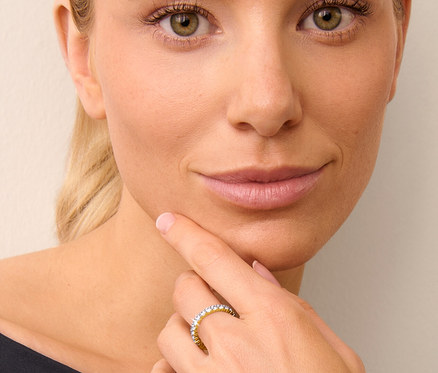 Une femme blonde touche son menton avec sa main, portant une bague mémoire dorée en argent 925.