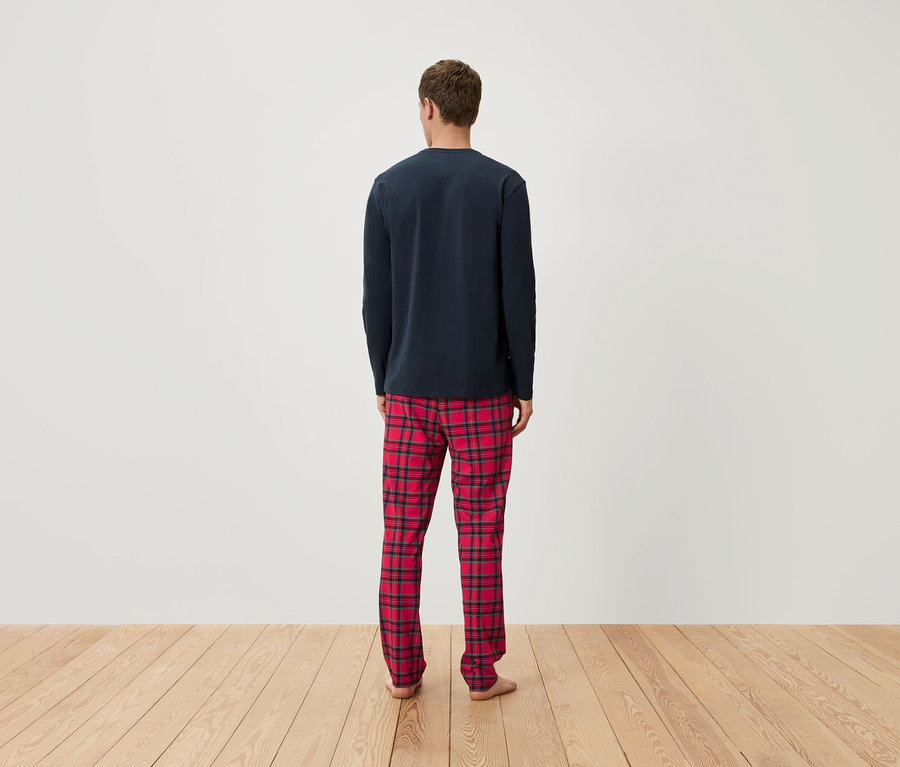 Un homme, vu de dos, porte un haut de pyjama bleu marine à manches longues et un pantalon de pyjama à carreaux rouges.