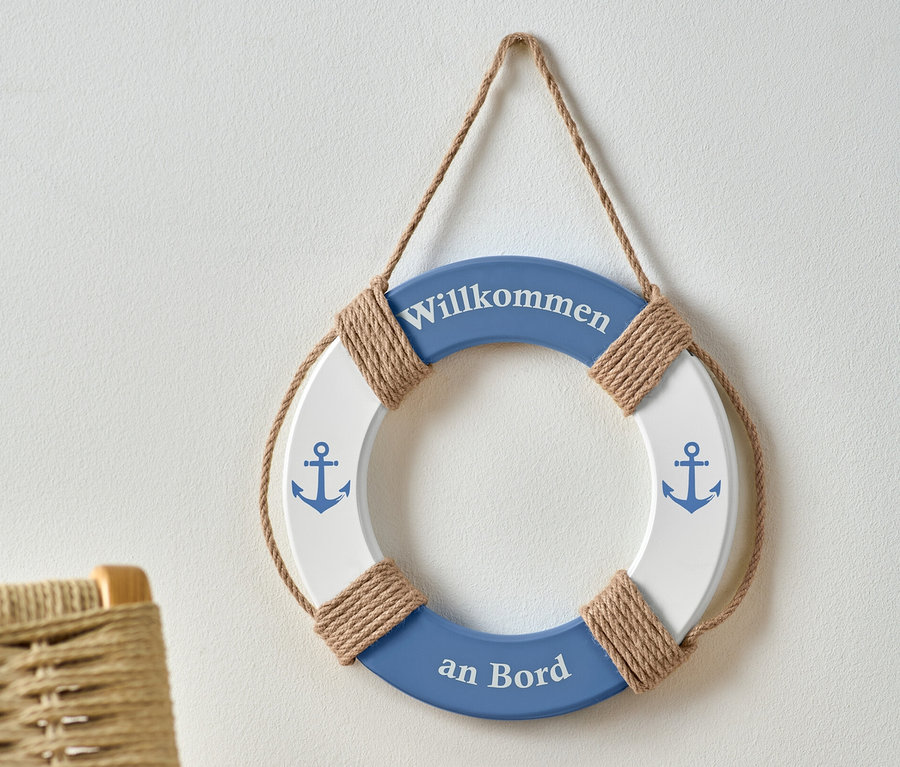 Une bouée de sauvetage décorative bleue et blanche avec l'inscription "Willkommen an Bord" et des images d'ancres est accrochée à un mur blanc.