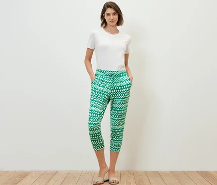 Une femme debout, les mains dans les poches, portant un pantalon 3/4 en jersey imprimé.