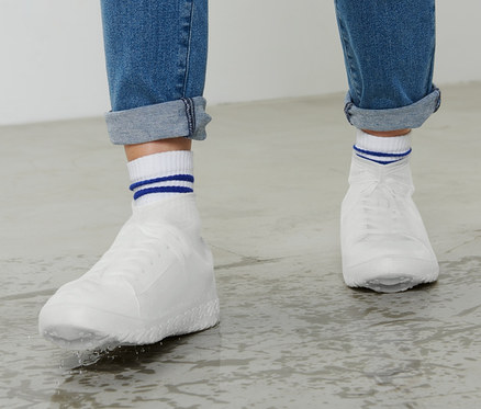 Des jambes portant un jean et des chaussures blanches avec des couvre-chaussures de pluie se tiennent sur un sol mouillé.