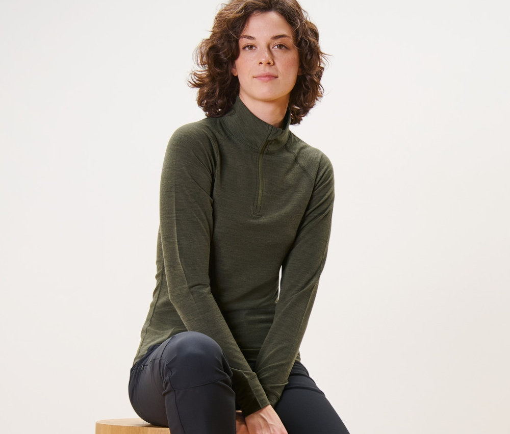 Une femme est assise sur des cylindres en bois et porte un t-shirt technique kaki avec de la laine certifiée RWS.