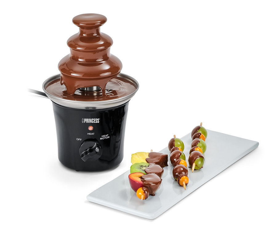 Mini-fontaine à chocolat électrique avec brochettes de fruits sur une assiette blanche.