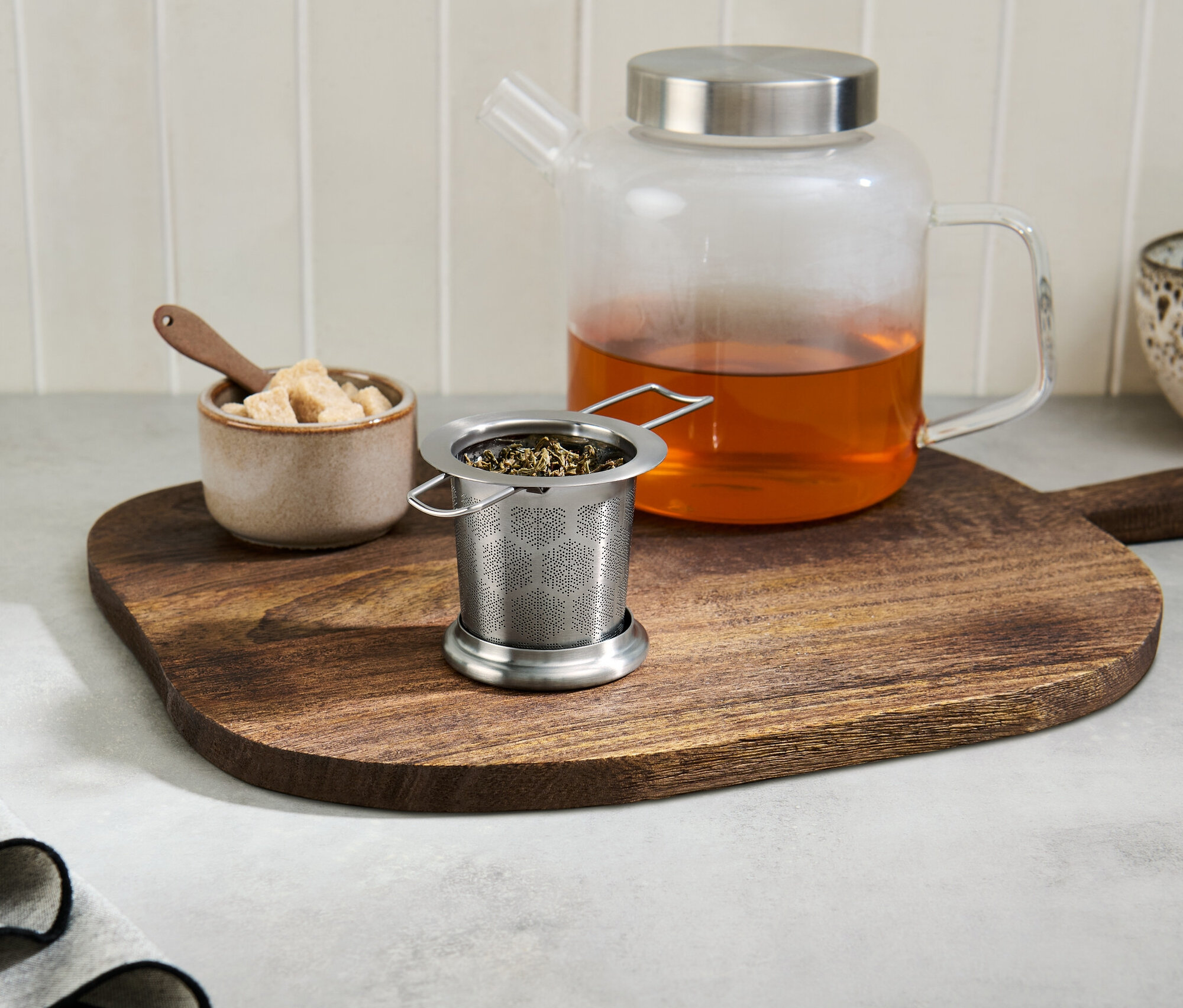 Passe-thé avec du thé sur une planche à découper en bois à côté d'une théière en verre avec du thé.