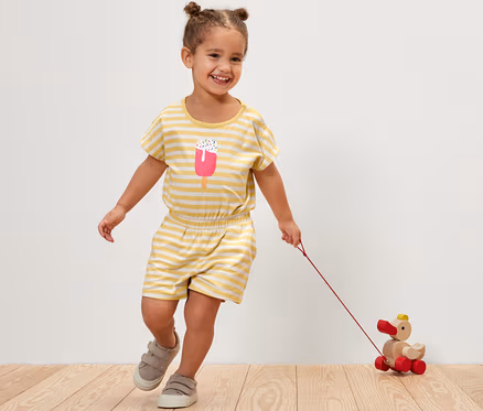 Fillette souriante en combinaison pour enfant rayée tirant un jouet en bois en forme de canard.