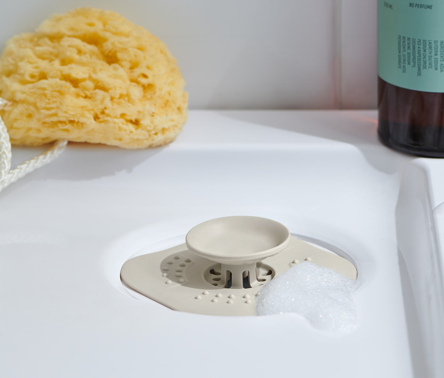 Un tamis / bonde d'écoulement est placé dans un lavabo, à côté duquel se trouvent une éponge de bain et, derrière, un flacon de gel douche.