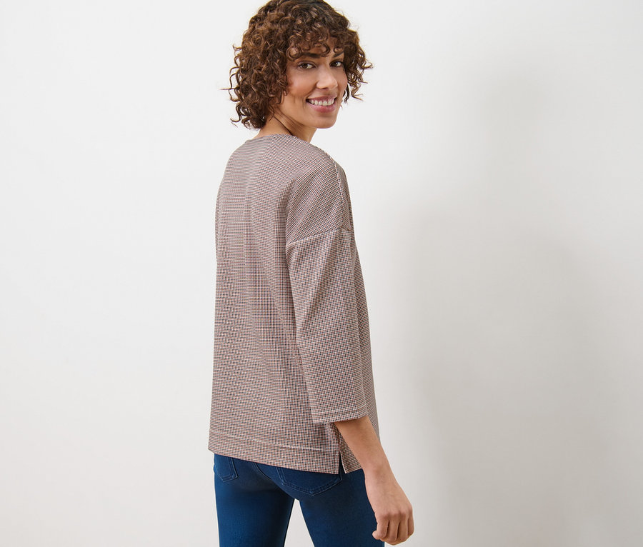 Une femme regardant par-dessus son épaule porte un sweat-shirt à carreaux et un jean.