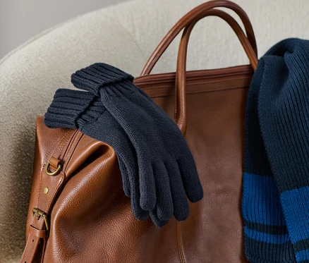 Des gants en maille sont posés sur un sac en cuir marron avec une écharpe en maille.