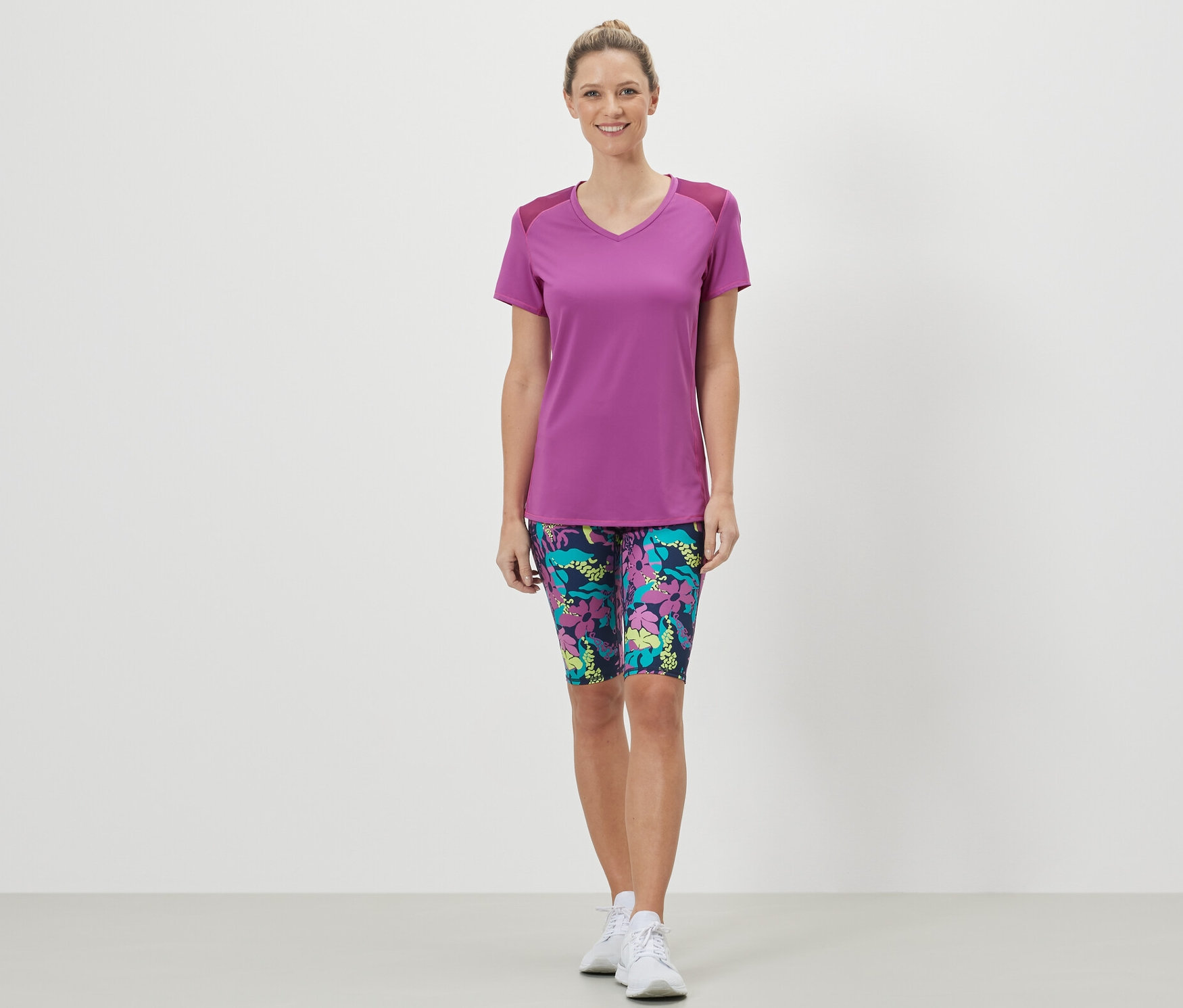 Une femme porte un t-shirt de sport et un short à fleurs.