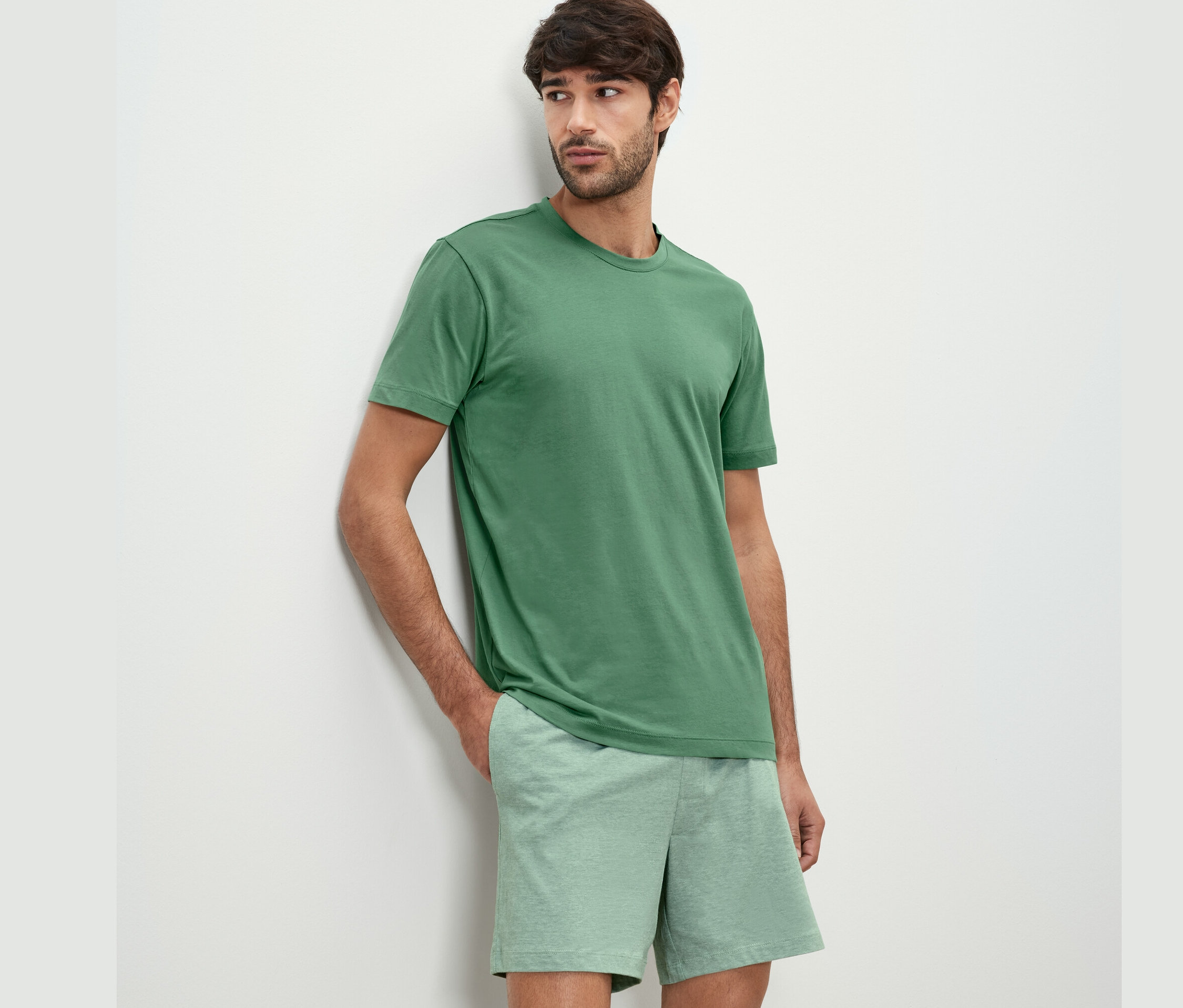 Homme appuyé contre un mur portant un ensemble pyjama shorty.