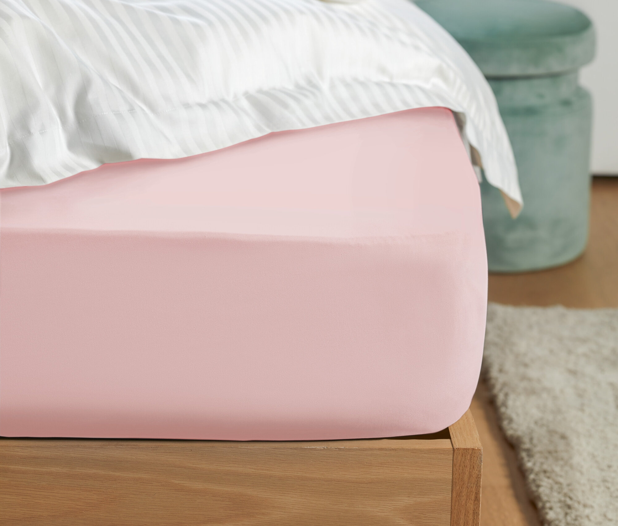 Gros plan d'un drap-housse rose sur un lit avec du linge de lit rayé blanc et un tabouret vert à l'arrière-plan.