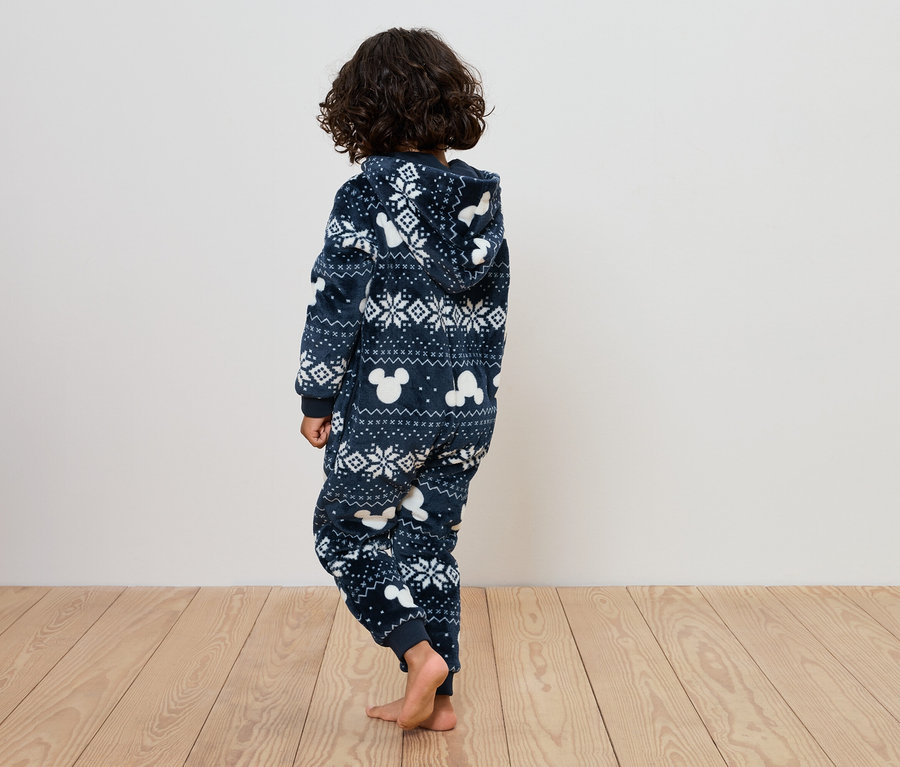 Un enfant debout, vu de dos, portant une combinaison bleue avec des motifs blancs.
