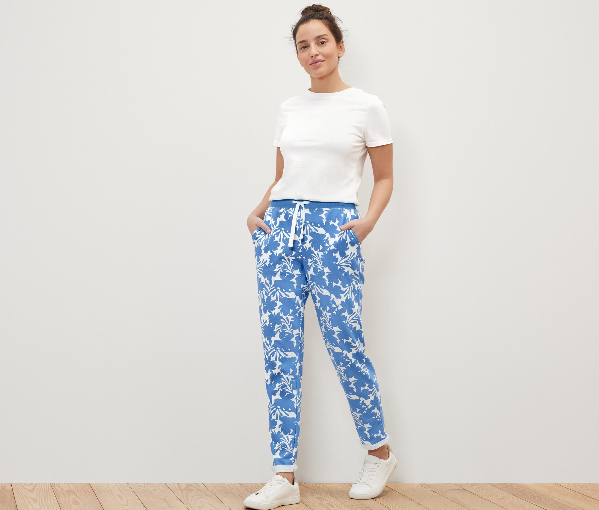 Une femme pose en pantalon molletonné imprimé, t-shirt blanc et baskets.