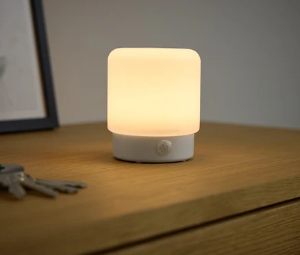 Une minilampe LED multifonction à détecteur de mouvement est allumée sur une table de chevet.