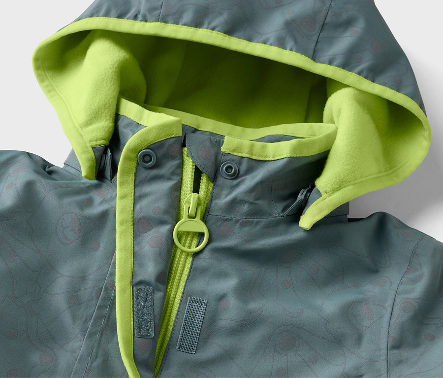 Gros plan sur une veste de pluie thermique pour enfant avec des éléments réfléchissants et une capuche bordée de vert néon.