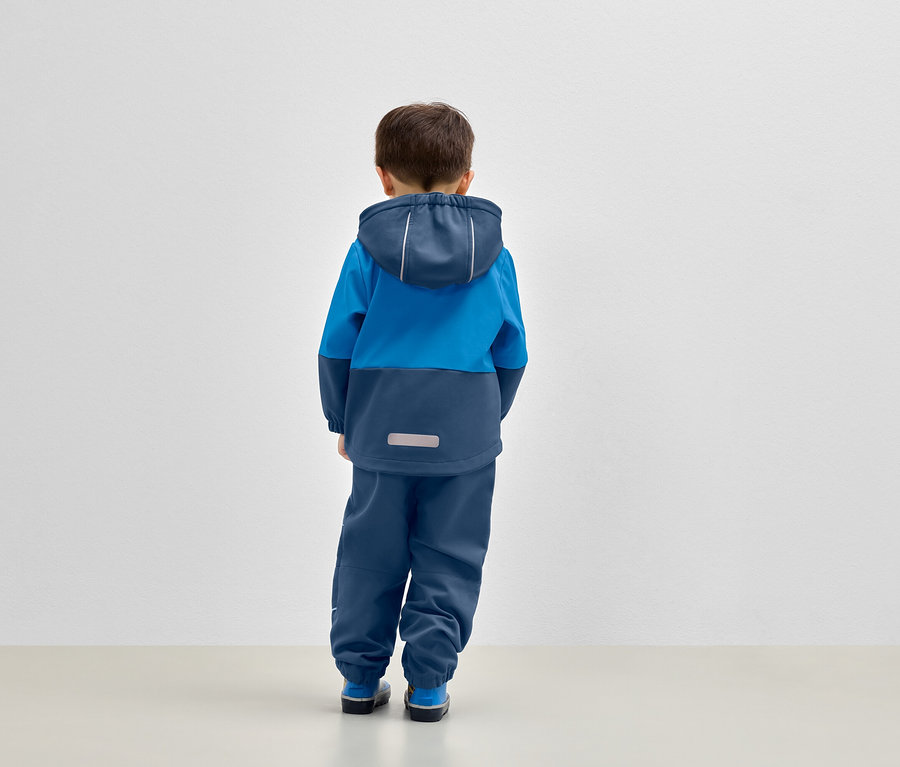 Un garçon se tient dos à l'objectif, portant une veste à capuche bleue et un pantalon bleu.