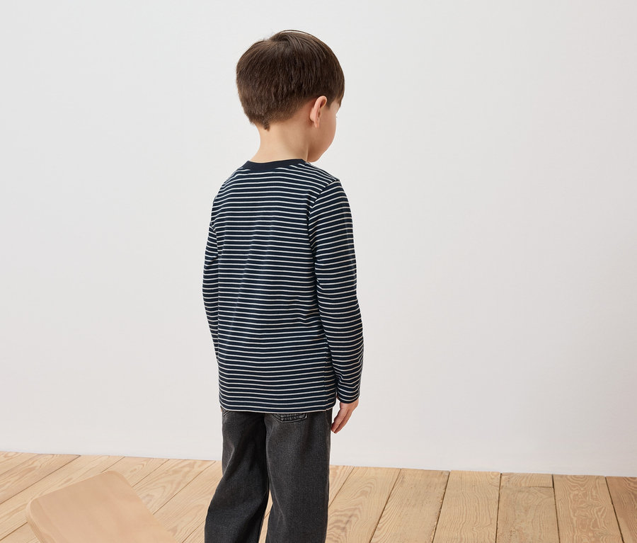 Un garçon se tient dos à la caméra, portant un t-shirt à manches longues rayé et un jean.