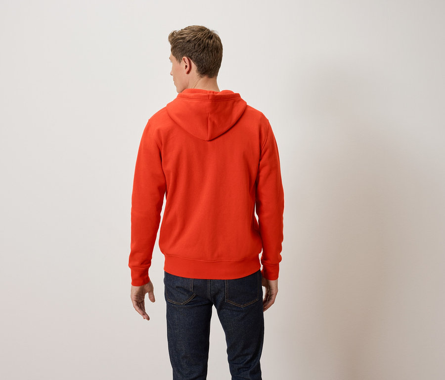 Un homme, vu de dos, porte un sweat à capuche orange et un jean bleu.