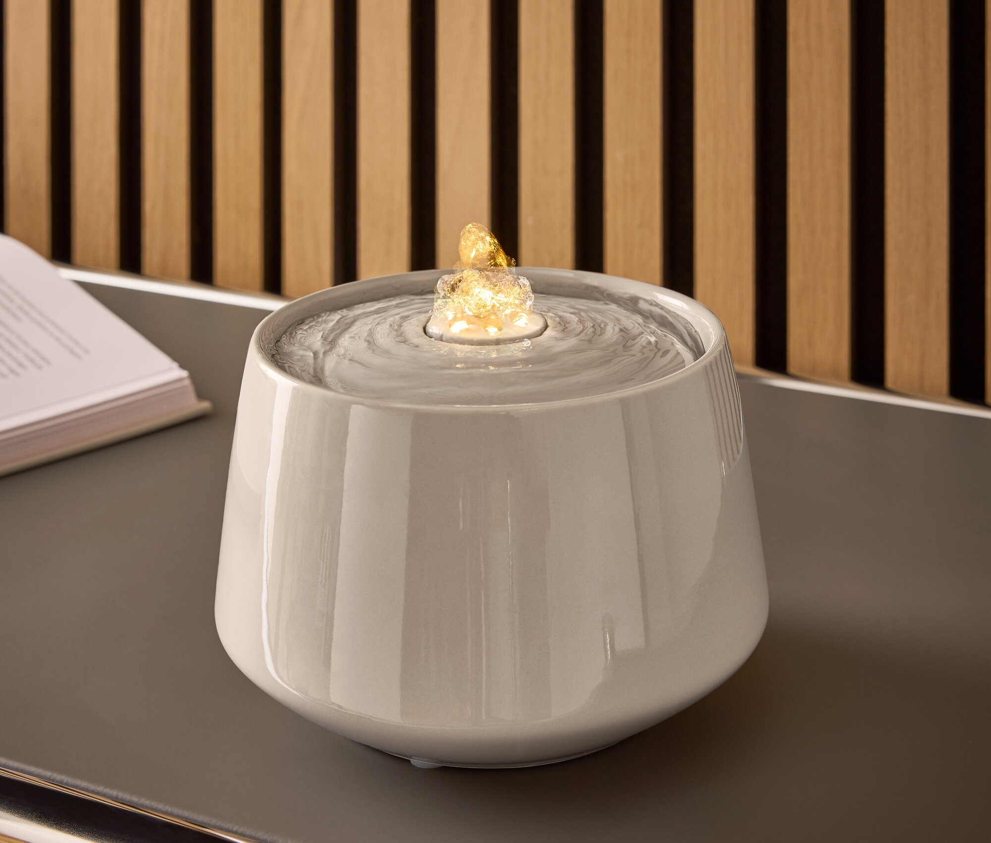 Fontaine en céramique grise avec de l'eau et une pierre éclairée sur une table grise.