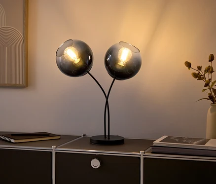 Deux lampes en verre avec des ampoules sur une commode noire.