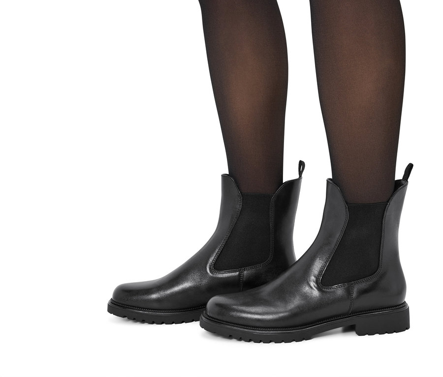 Jambes en collants noirs portant des bottines Chelsea en cuir noir sur fond blanc.