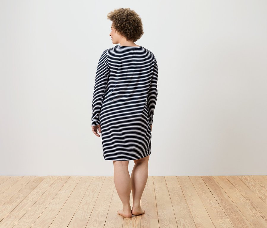 Une femme se tient dos à la caméra, portant une robe à manches longues rayée bleu et blanc.