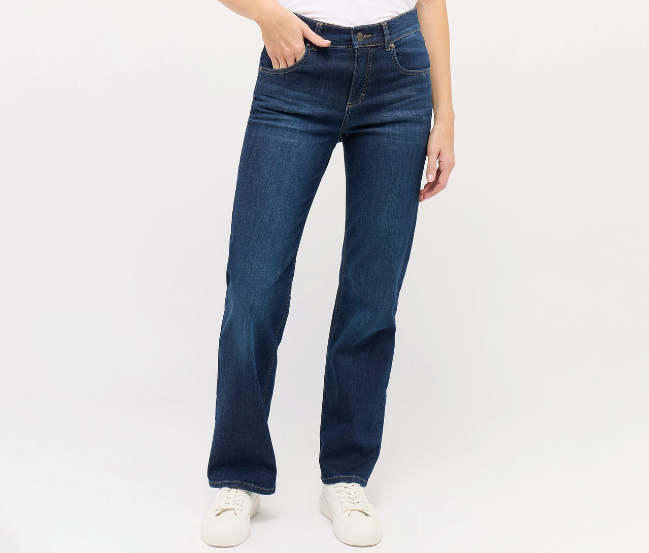 Une femme porte un jean Angels « Lara » coupe droite bleu foncé et des baskets blanches.