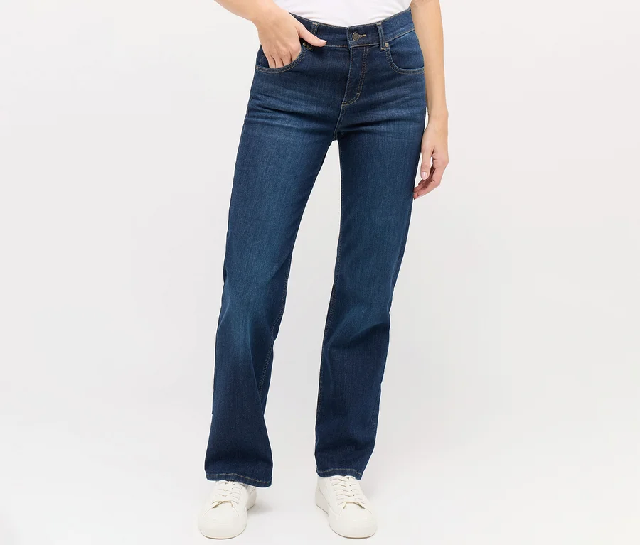 Une femme porte un jean Angels « Lara » coupe droite bleu foncé et des baskets blanches.