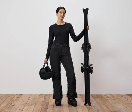 Femme en tenue de ski noire tenant des skis et un casque.