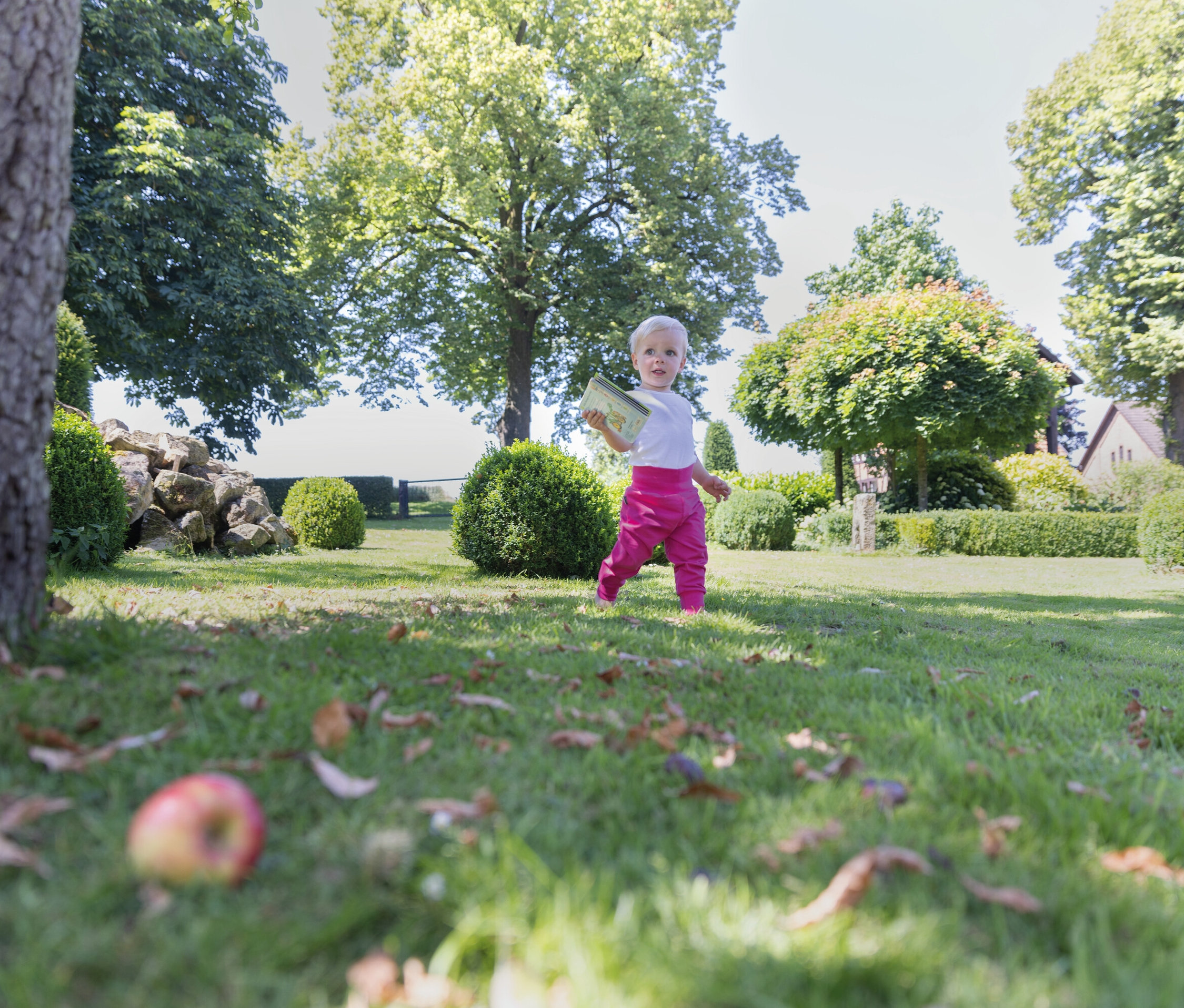Un enfant en pantalon rose marche sur l'herbe dans un jardin.