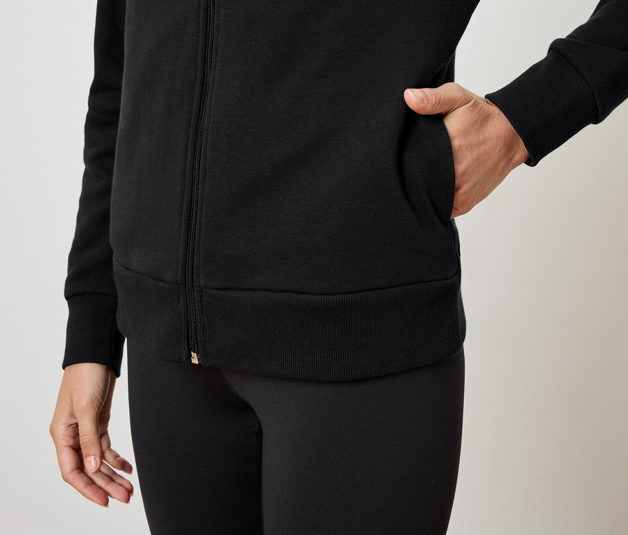 Une femme a sa main dans la poche d'un sweat-shirt noir à fermeture éclair et porte un legging noir.