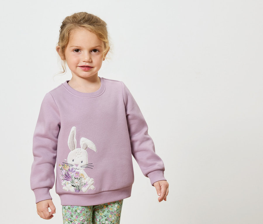 Fillette portant un sweat-shirt lilas avec un motif de lapin et de fleurs.