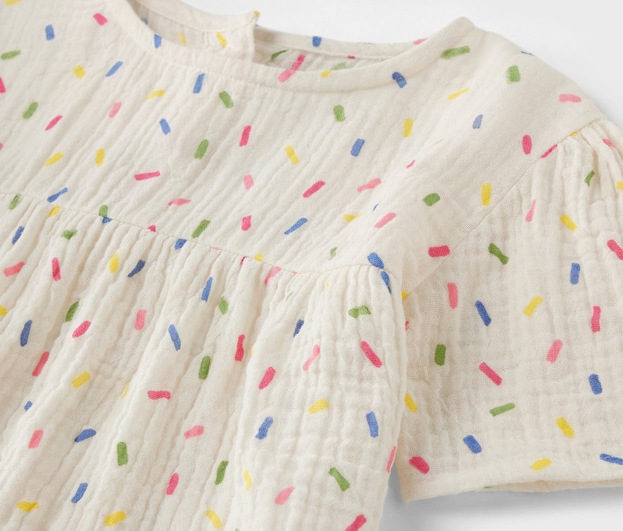 Détail d'une blouse en mousseline pour enfant avec des motifs colorés.