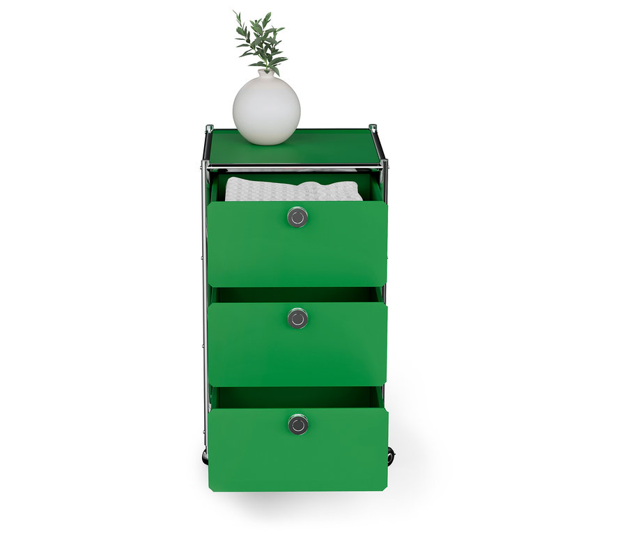 Système de rangement modulaire vert avec trois tiroirs, dont un ouvert avec des vêtements blancs, sur le dessus un vase blanc avec une plante.