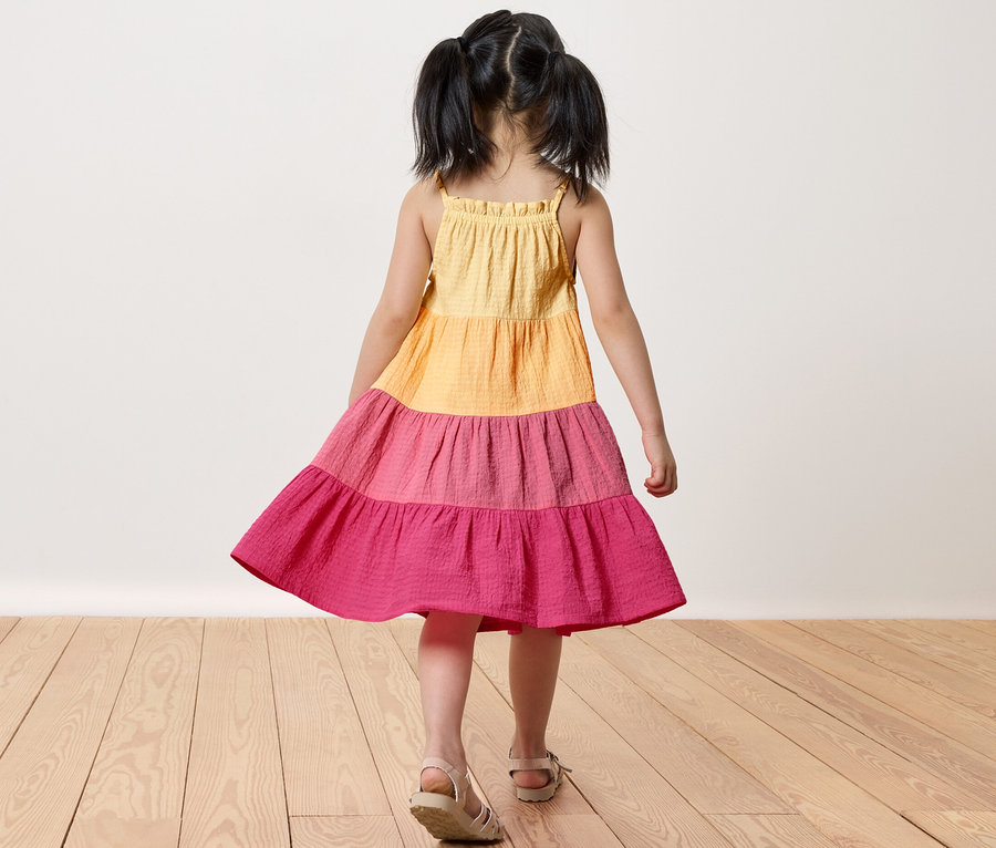 Fillette en robe tissée pour enfant debout sur un plancher en bois.