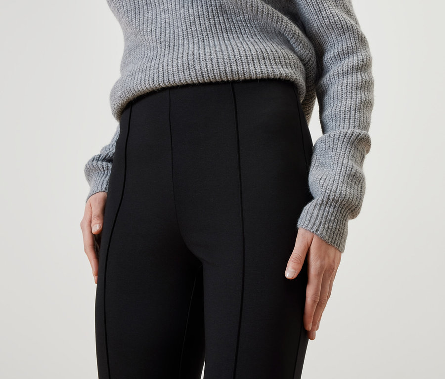 Gros plan d'une femme portant un pantalon noir et un pull gris.