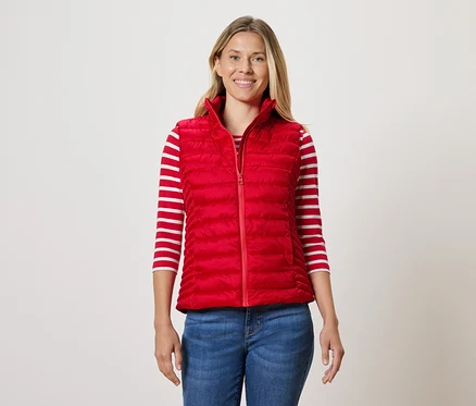 Une femme porte une veste matelassée rouge, un T-shirt rayé et un jean.