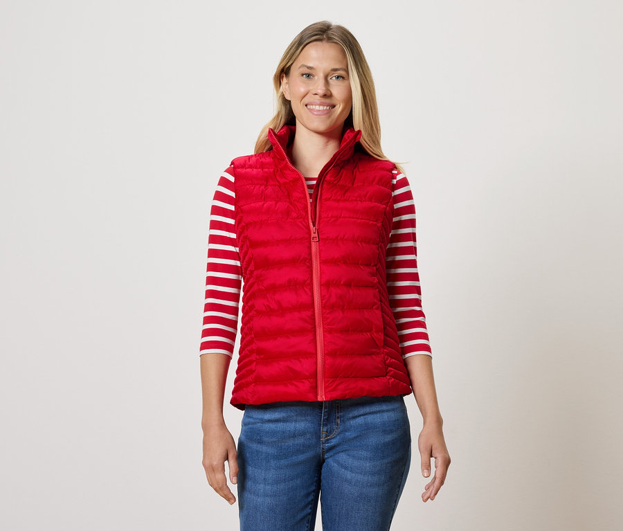 Une femme porte une veste matelassée rouge, un T-shirt rayé et un jean.