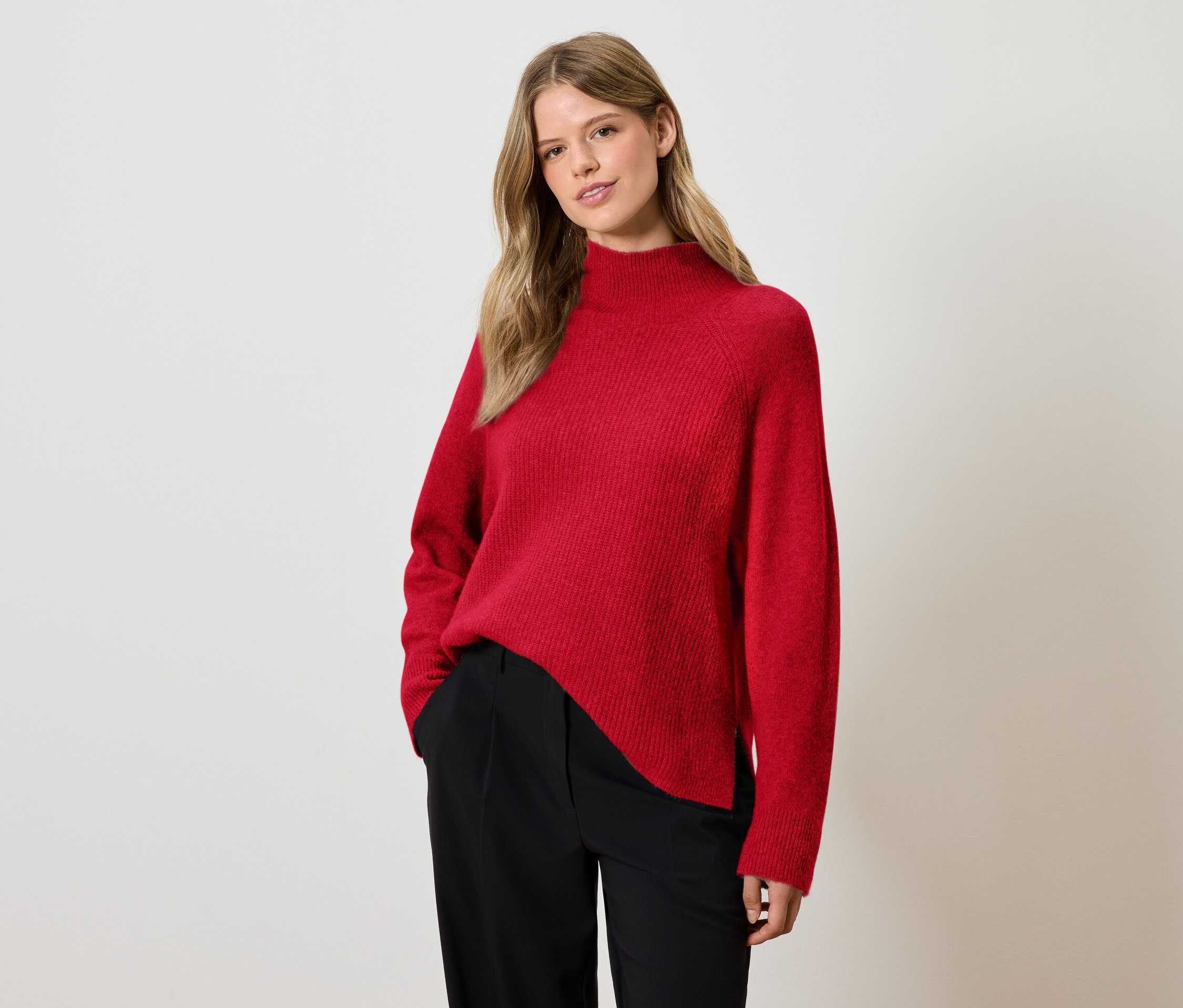 Femme posant en pull rouge et pantalon noir.