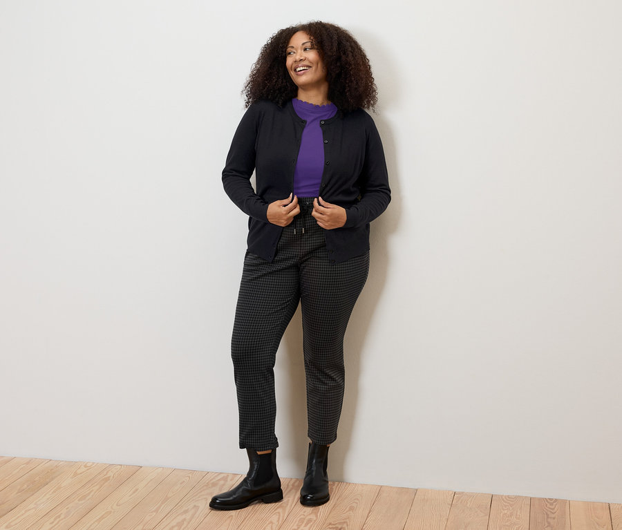 Une femme portant un t-shirt lilas à bordure ondulée, un pantalon foncé et un cardigan.