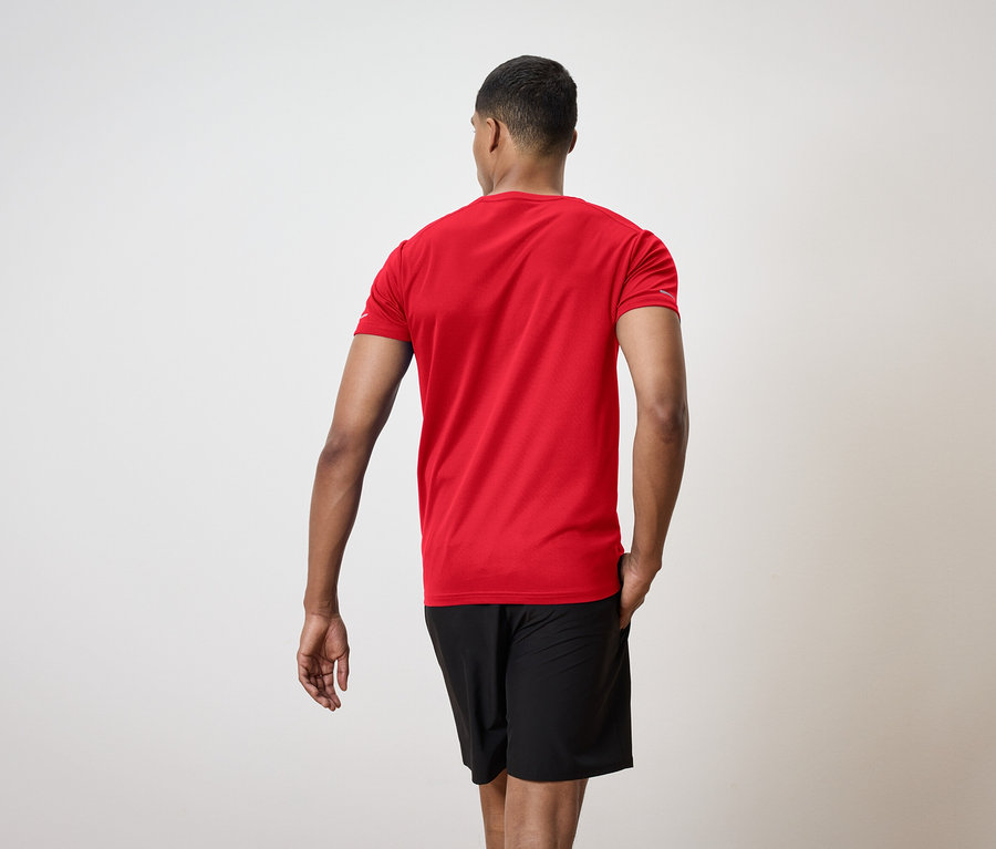 Un homme dos à la caméra portant un t-shirt rouge et un short noir.