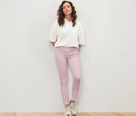 Une femme debout porte un jean coloré coupe «	Emma	» et un chemisier blanc.